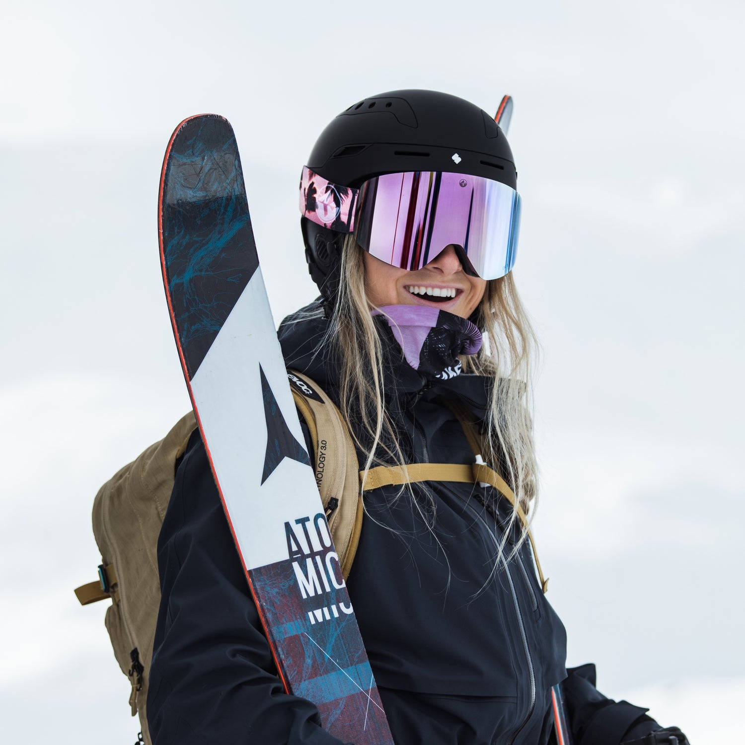 Eine junge Skifahrerin lacht in die Kamera, sie hält ihre Ski in den Händen und trägt eine große lila Skibrille; Credits: Florian Dorn