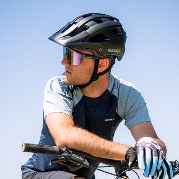 Mann mit einem NAKED Optics Mountainbike-Helm und einer Sonnenbrille, der auf einem Fahrrad sitzt und zur Seite in den klaren Himmel blickt.