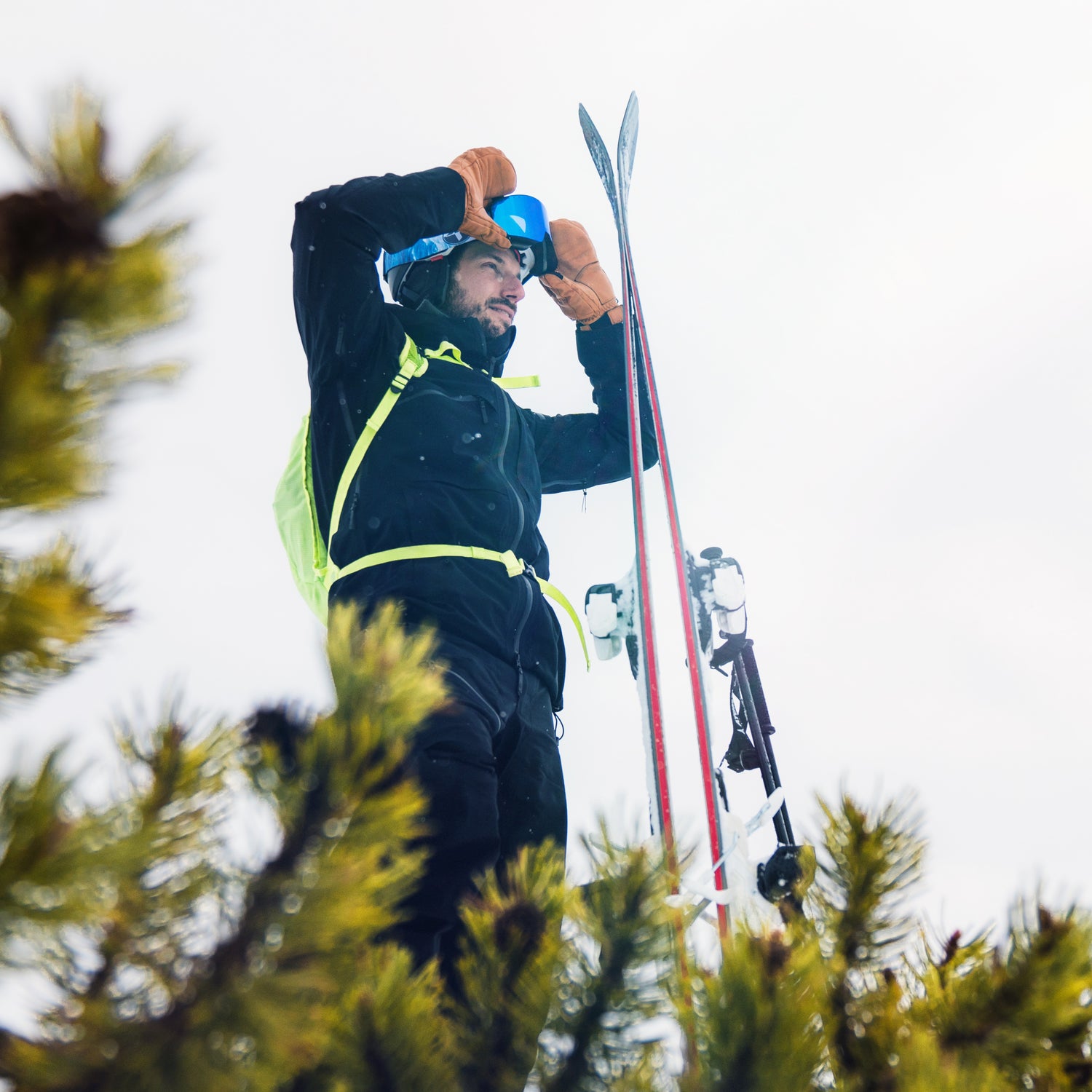 Ein Skifahrer steht auf einer Erhöhung und schaut in die Ferne. Dabei zieht er sich seine Skibrille vom Helm ins Gesicht; Credits: Elias Neier