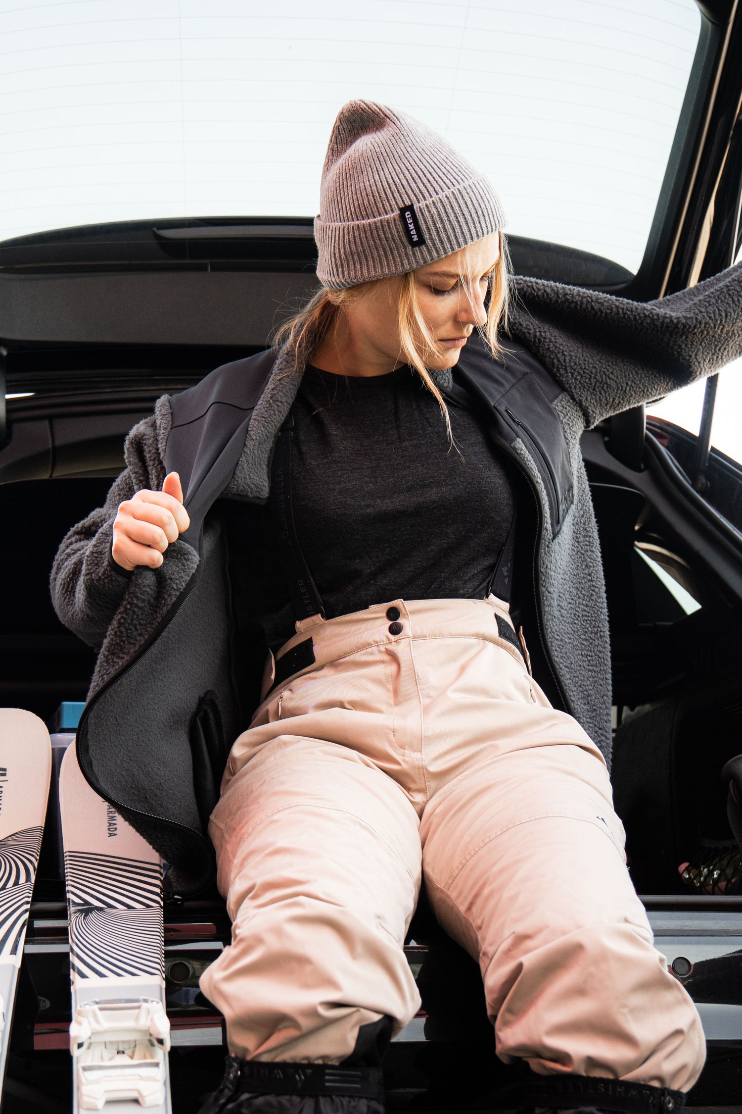 Eine junge Frau macht sich zum Skifahren fertig und zeiht sich eine Skifleecejacke an; Credits: Elias Neier