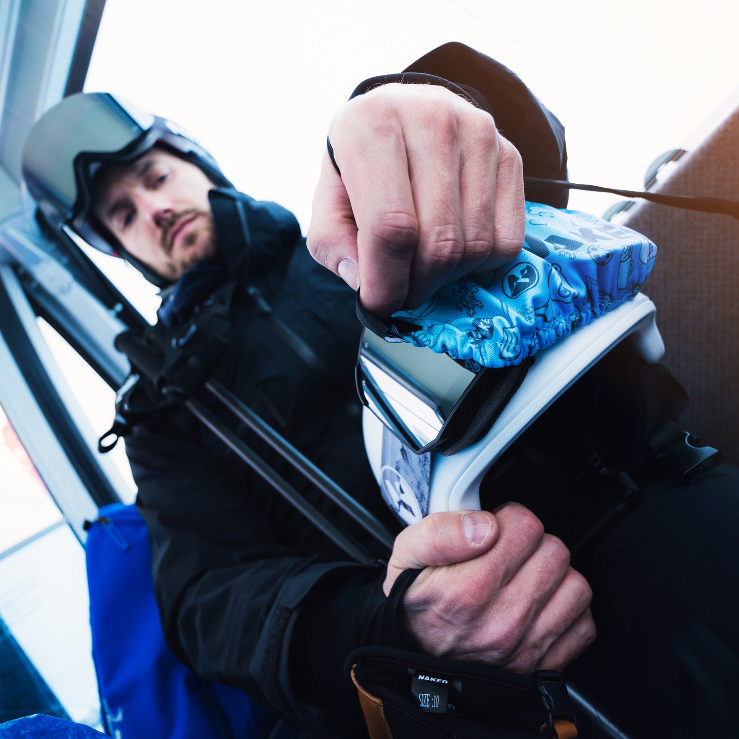 Ein Skifahrer sitzt in einer Gondel und bedeckt seine Skibrille mit einem Skibrillenschutz; Credits: Elias Neier