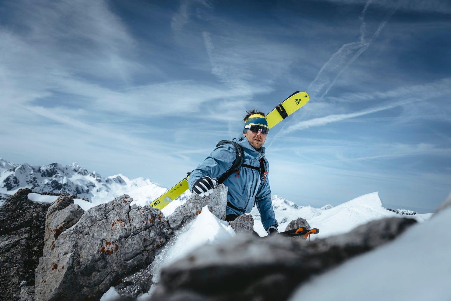Ein Mann klettert auf einem Getscher, er trägt seine Ski auf den Rucksack geschnallt und eine Gletscherbrille um seine Augen zu schützen; Credits: Patrick Bätz