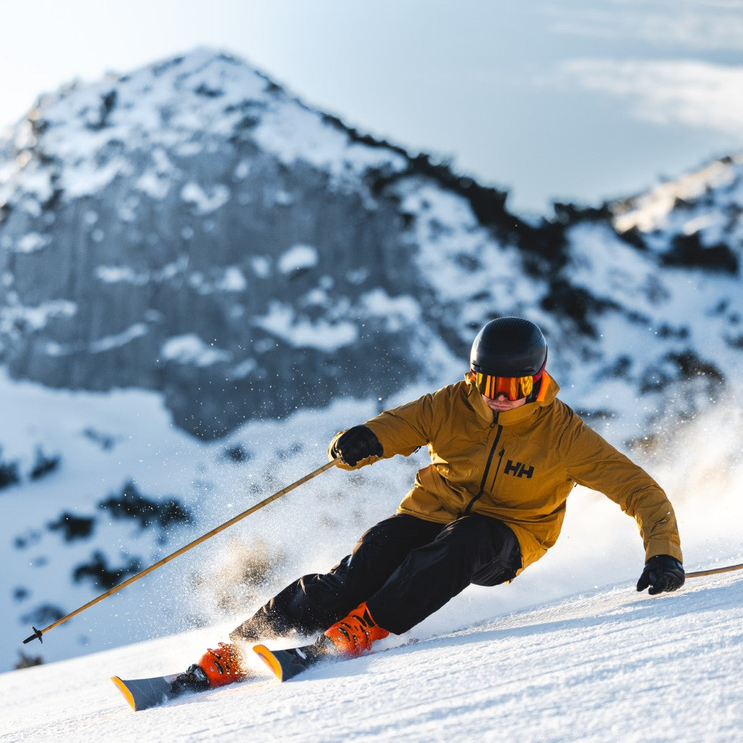 Ein Mann fährt Ski auf deiner Piste vor einem vershcneiten Berg, er lehnt sich weit in ide Kurfe; Credits: Mathäus Gartner
