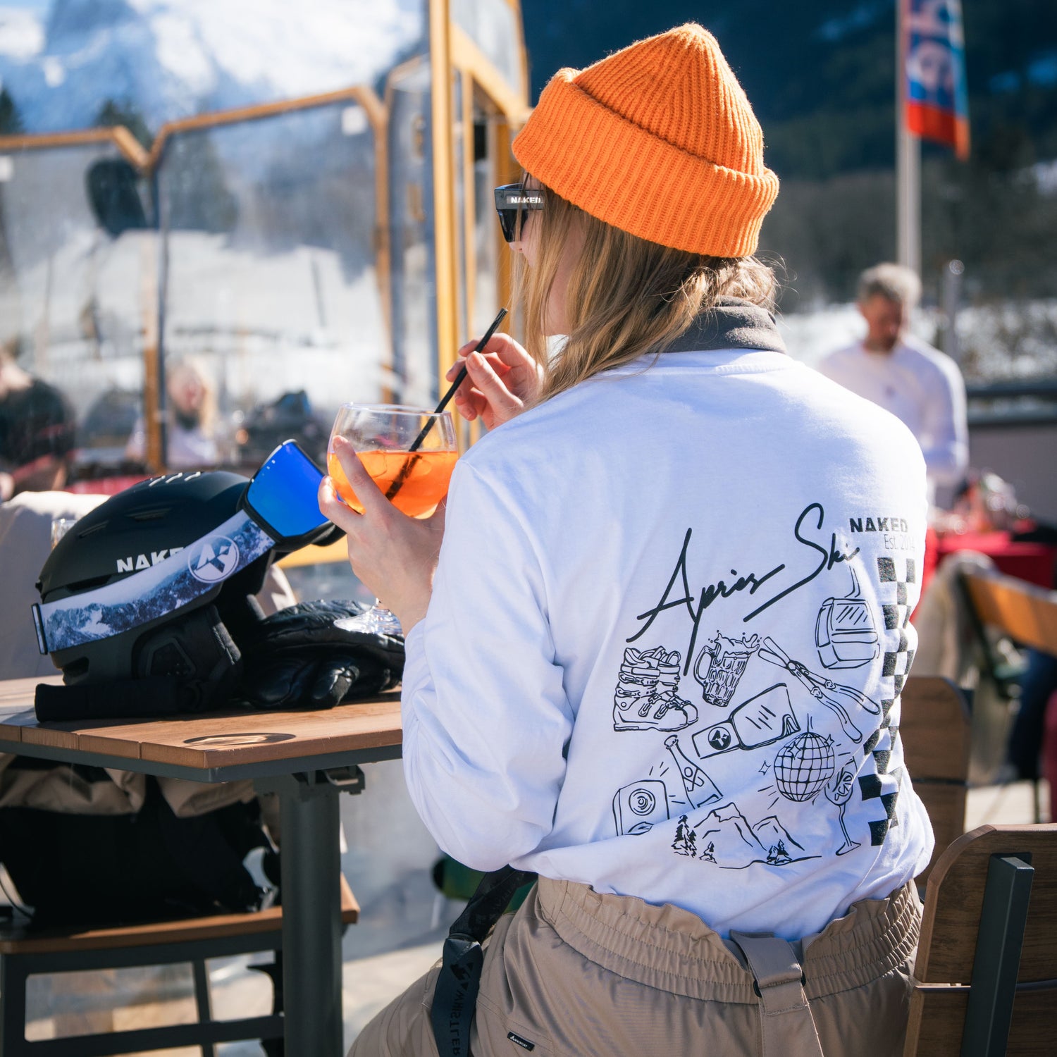 Eine Frau sitzt mit einem Cocktail in einer Après Ski Bar, sie trägt ein passendes T-Shirt mit Après Ski Design; Credits: Elias Neier